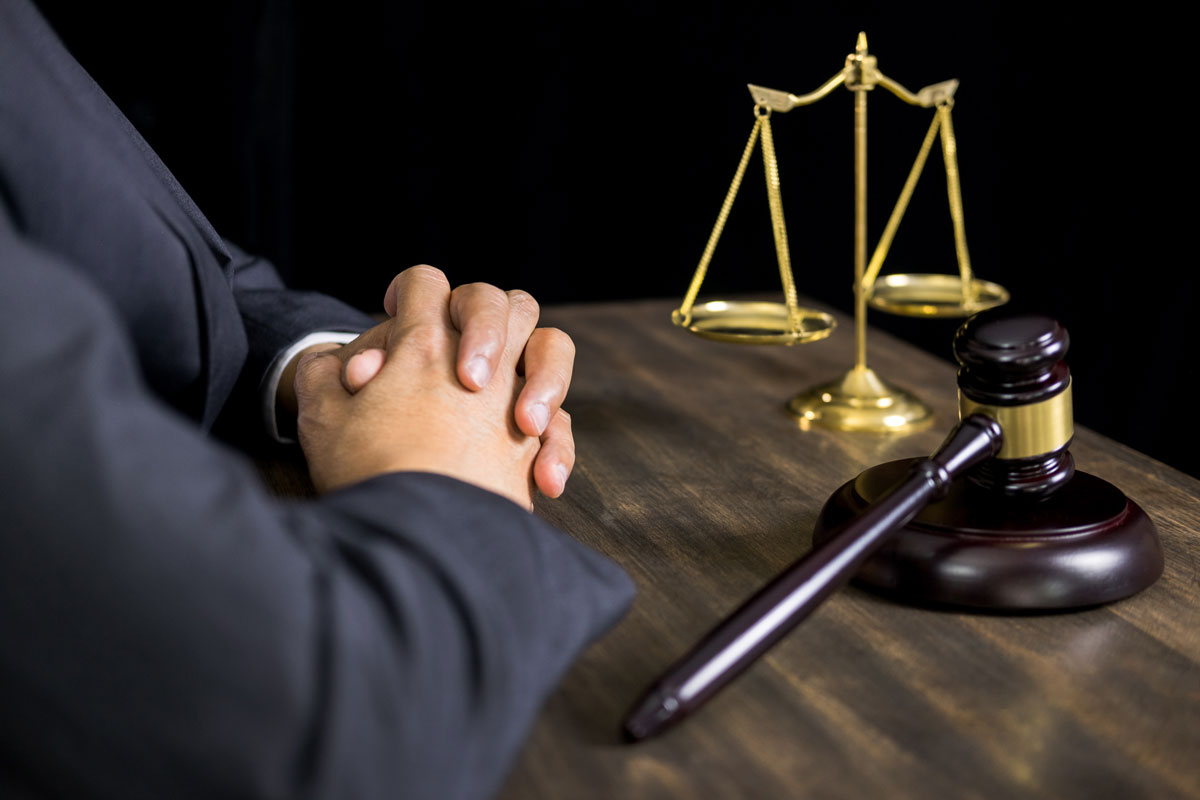 Juiz com mãos unidas, perto do malhete e balança da justiça em cima da mesa